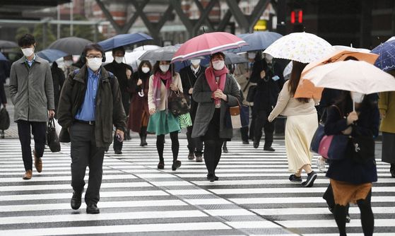 지난 4월 13일 오전 일본 도쿄도 지요다구 소재 도쿄역 인근 횡단보도에서 마스크를 쓴 사람들이 우산을 쓰고 길을 건너고 있다. 연합뉴스