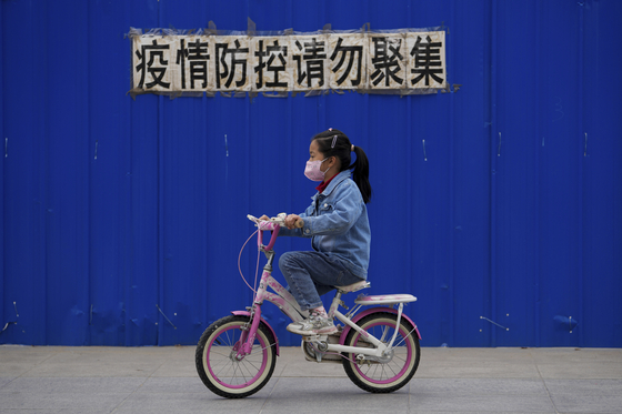 17일 베이징의 한 거주 지역에서 &#34;방역을 위해 모이지 마시오&#34; 라고 쓰인 통보문 아래로 마스크를 한 아이가 자전거를 타고 지나가고 있다. 〈사진=AP, 연합뉴스〉