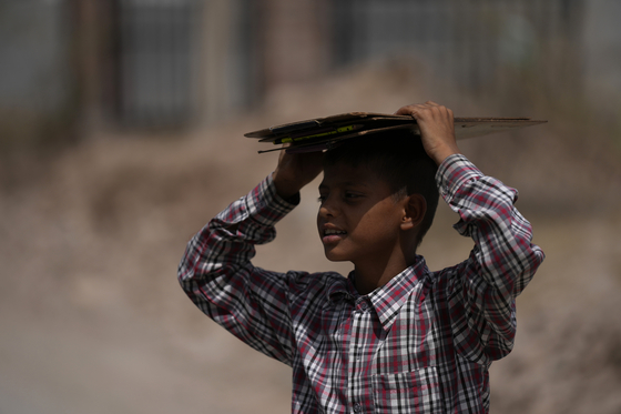 지난 19일 인도 잠무에서 학교에서 돌아온 한 소년이 햇빛을 피하기 위해 판지로 머리를 가리고 있다. 〈사진=AP 연합뉴스〉